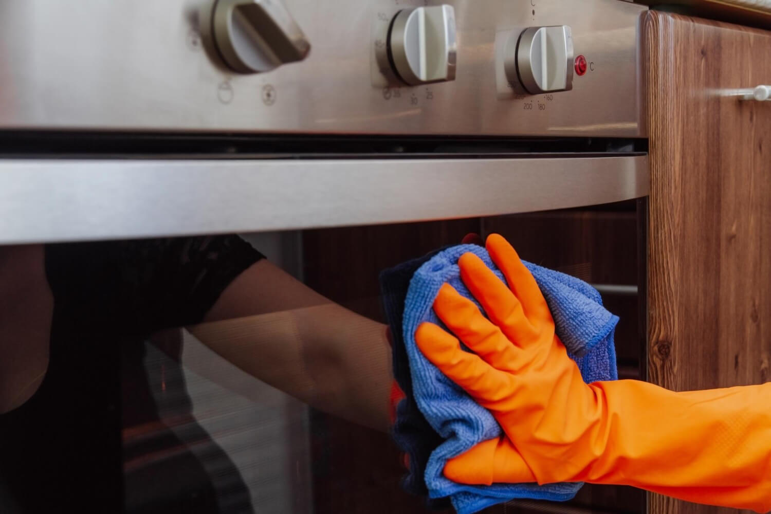 orangegloved hand with microfiber cleaning cloth wipes the outside of an electric oven
