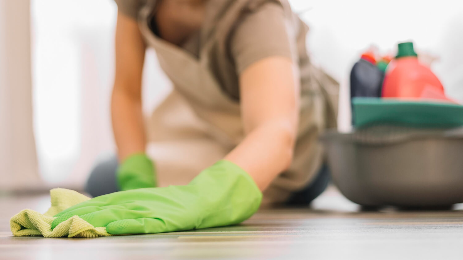 female cleaner in uniform close up cleaning floor in green gloves with yellow cloth and cleaning equipment next to her