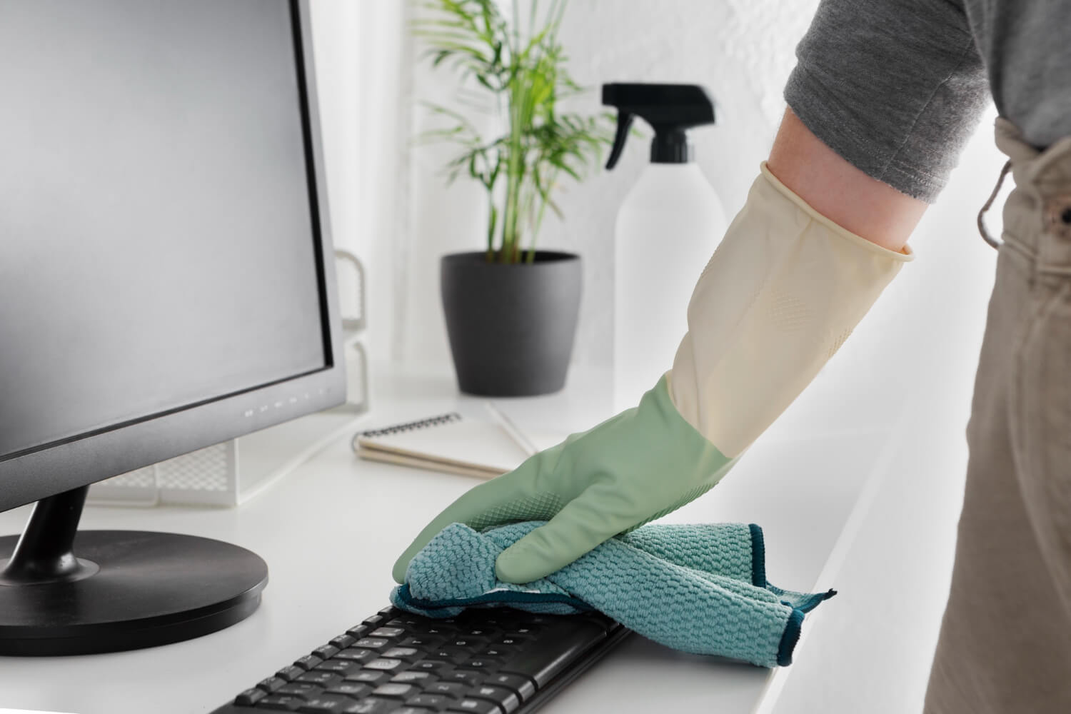 close up male hand in green protective glove cleaning keyboard with blue cloth