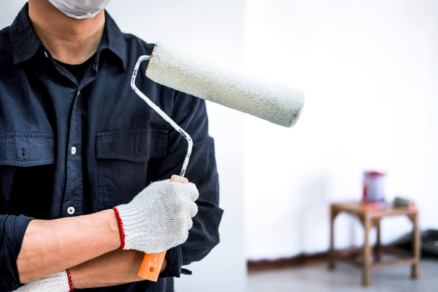 cropped handyman with arm crossed holding paint roller