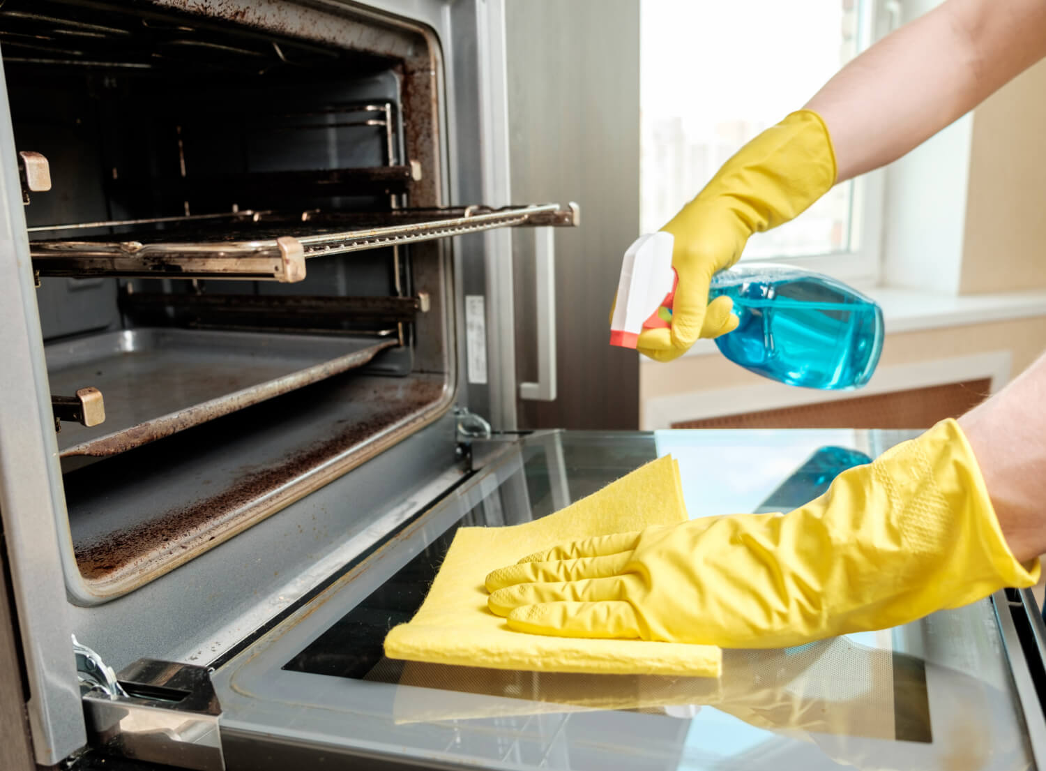 man holding bottle spray and rar while cleaning oven