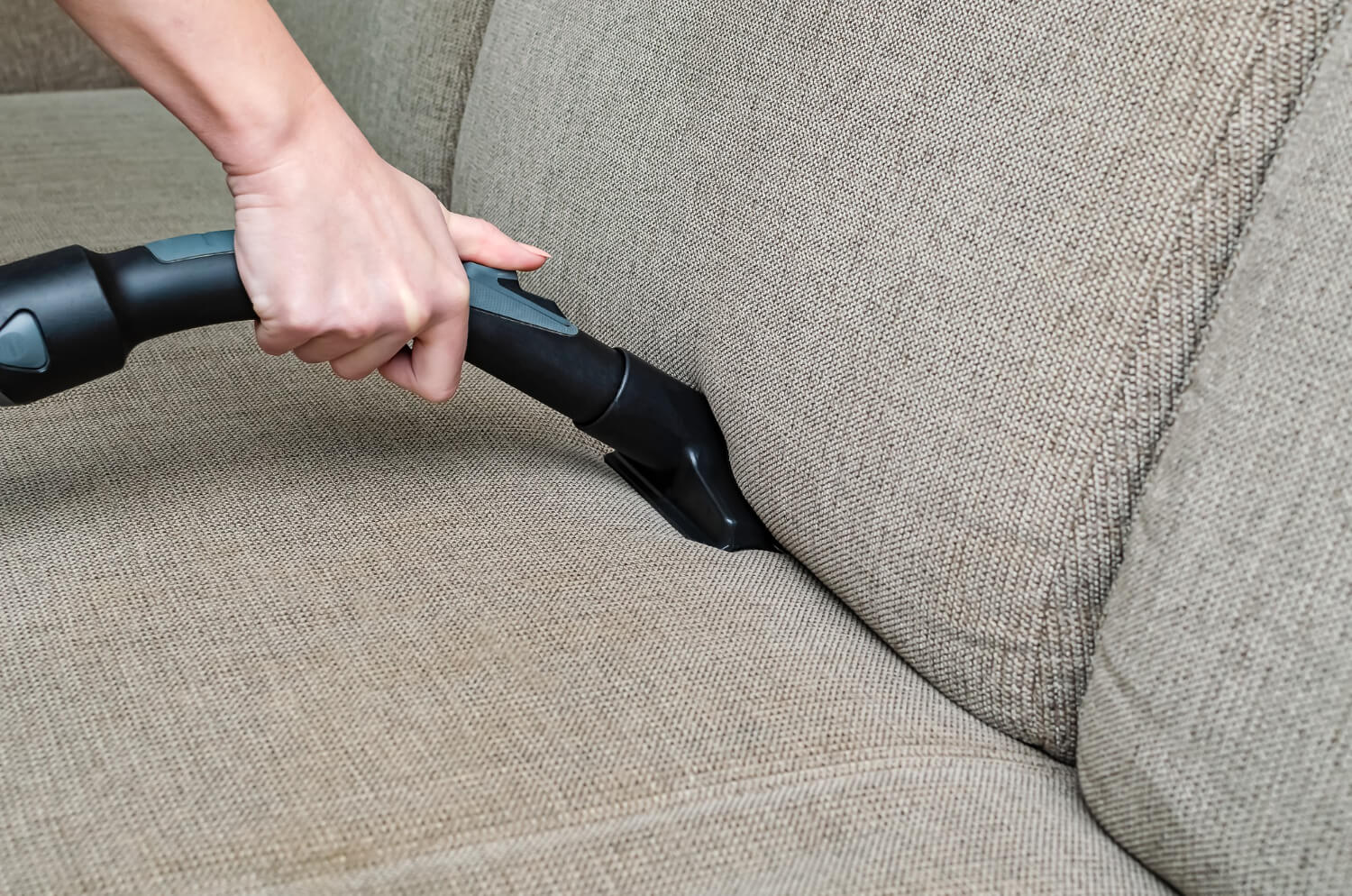 close up cropped female hand holding professional vacuum and cleaning sofa