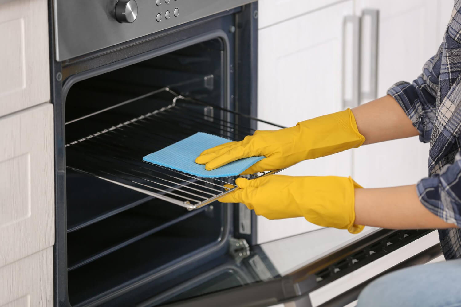 woman's hands with yellow gloves cleaning oven door close up>

<div class=