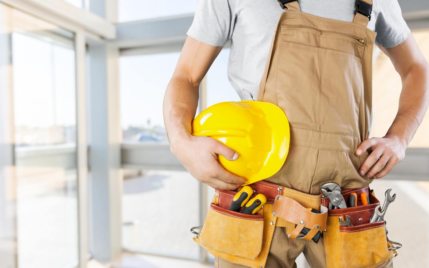 cropped handyman with tool belt holding yellow helmet