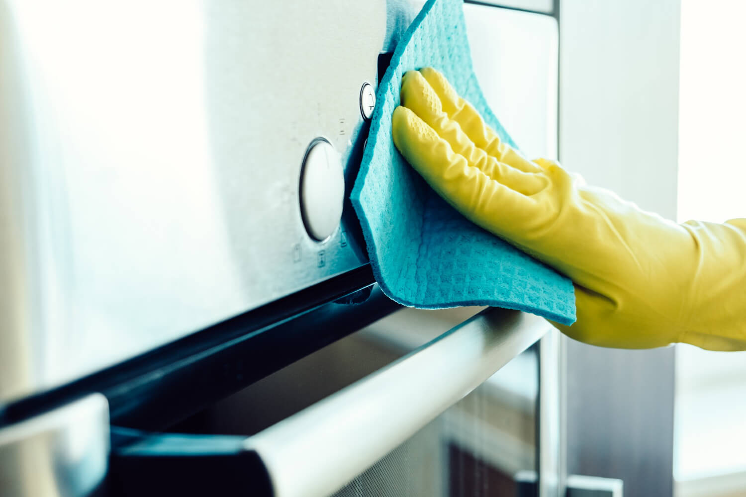 close up female hand in yellow gloves cleaning kitchen appliance with blue cloth