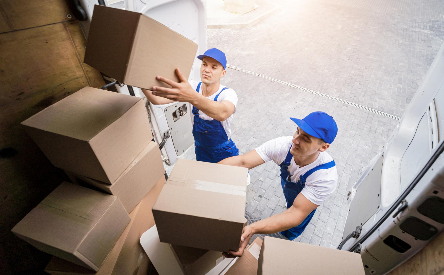 top view of two movers loading moving boxes in the back of a white van