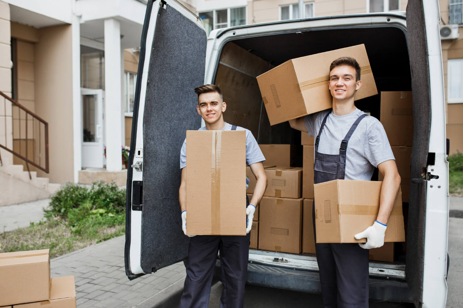 two movers in uniform standing in the back of white moving van holding moving boxes