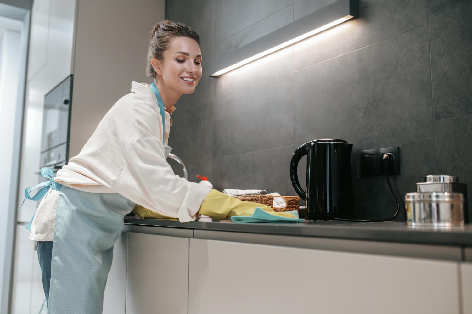 yoyng dark haired woman in yellow gloves cleaning kitchen surface with blue cloth