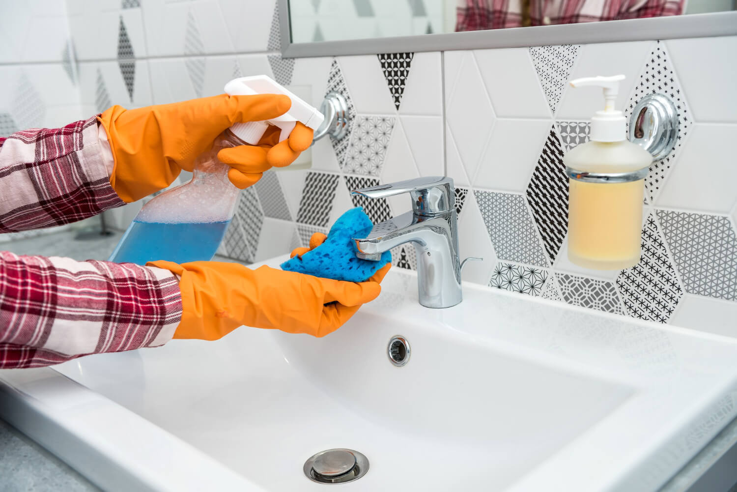 close up female cleaner hands in orange protective gloves cleaning bathroom sink with blue sponge and cleaning spray
