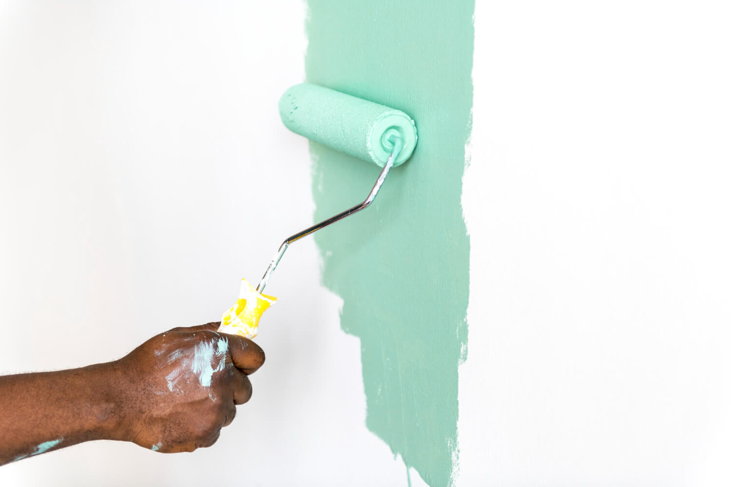 mans hand painting white wall blue with paint roller