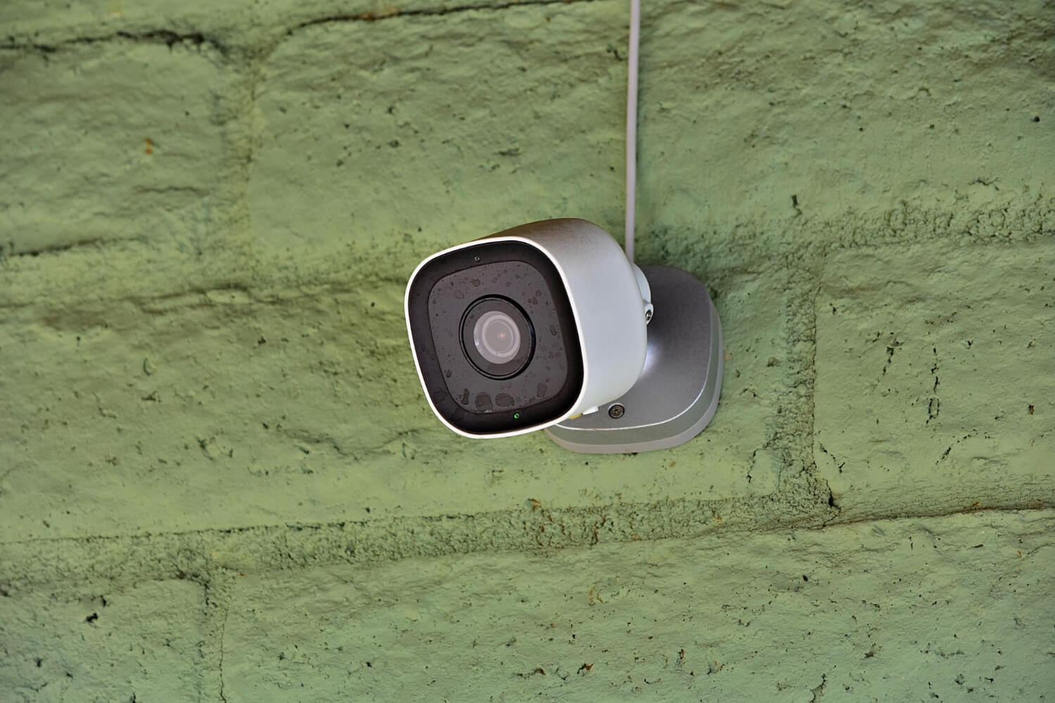 home security camera installed on green wall outdoors