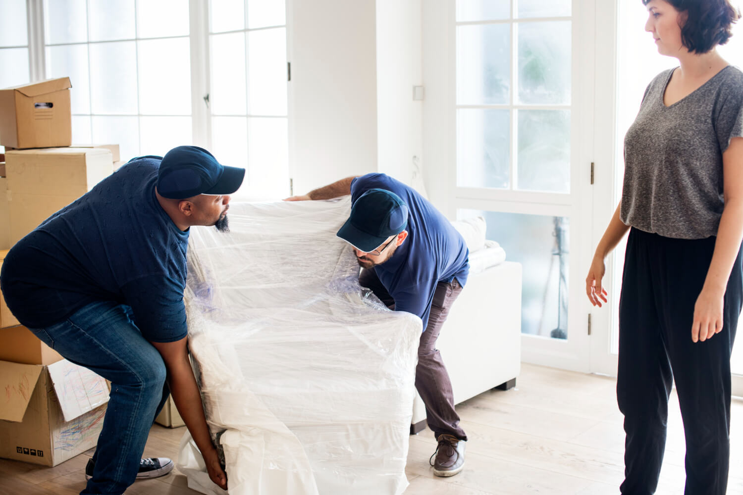 two movers picking up wrapped chair while female homeowner is looking at them