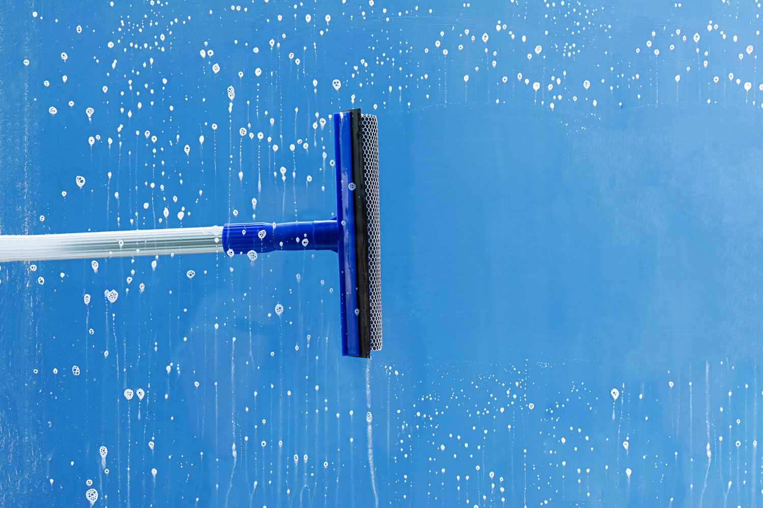close up cleaning brush cleaning stripe of soaped window with blue backround