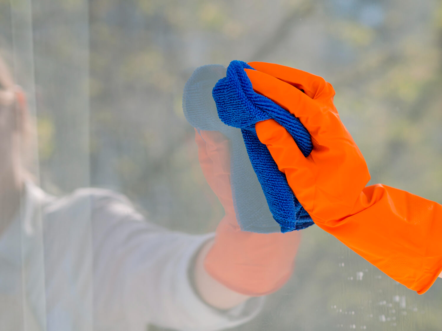close up hand with orange glove holding blue cloth while cleaning window