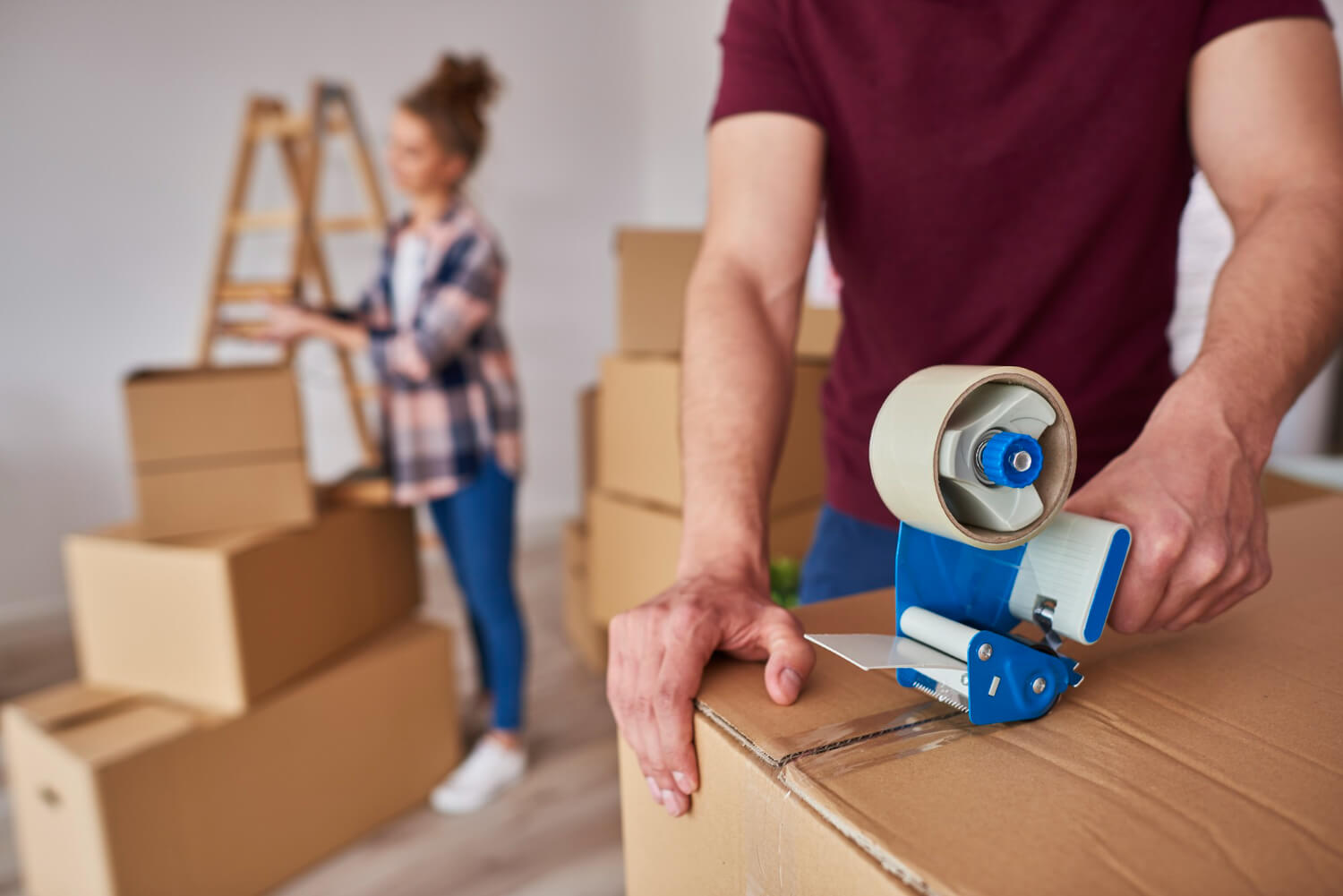 man with adhesive tape packing boxes in the front and blurry woman packing in the back