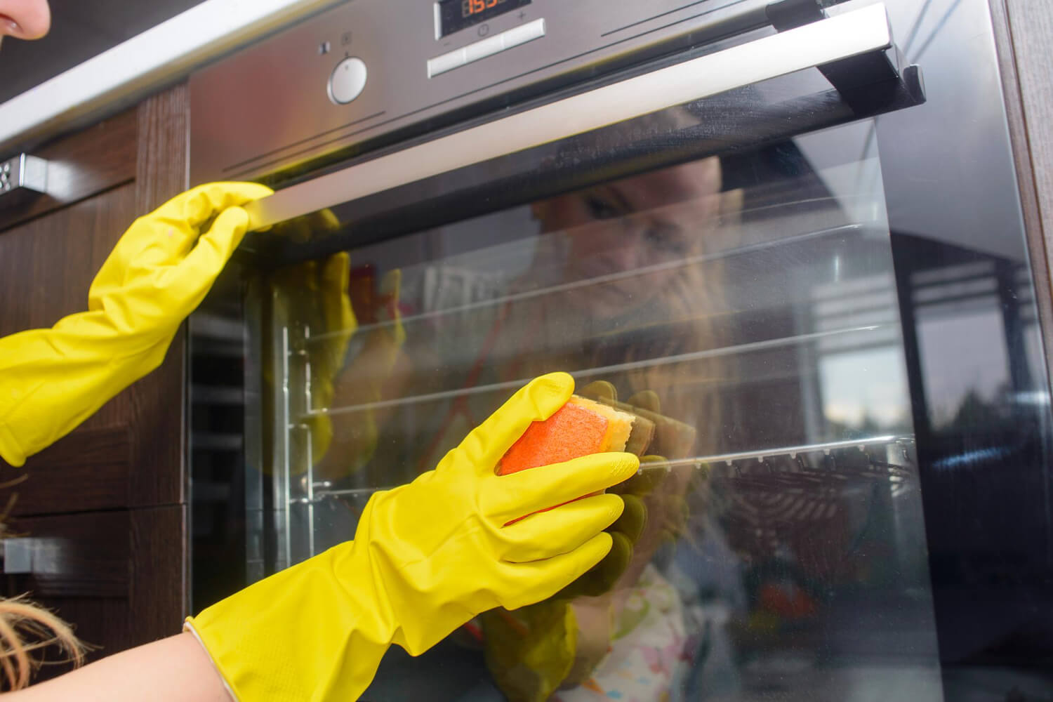 woman cleaning the door of oven with yellow sponge