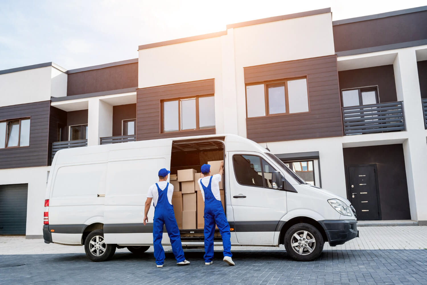 two removal company workers unloading boxes from white van nto new home