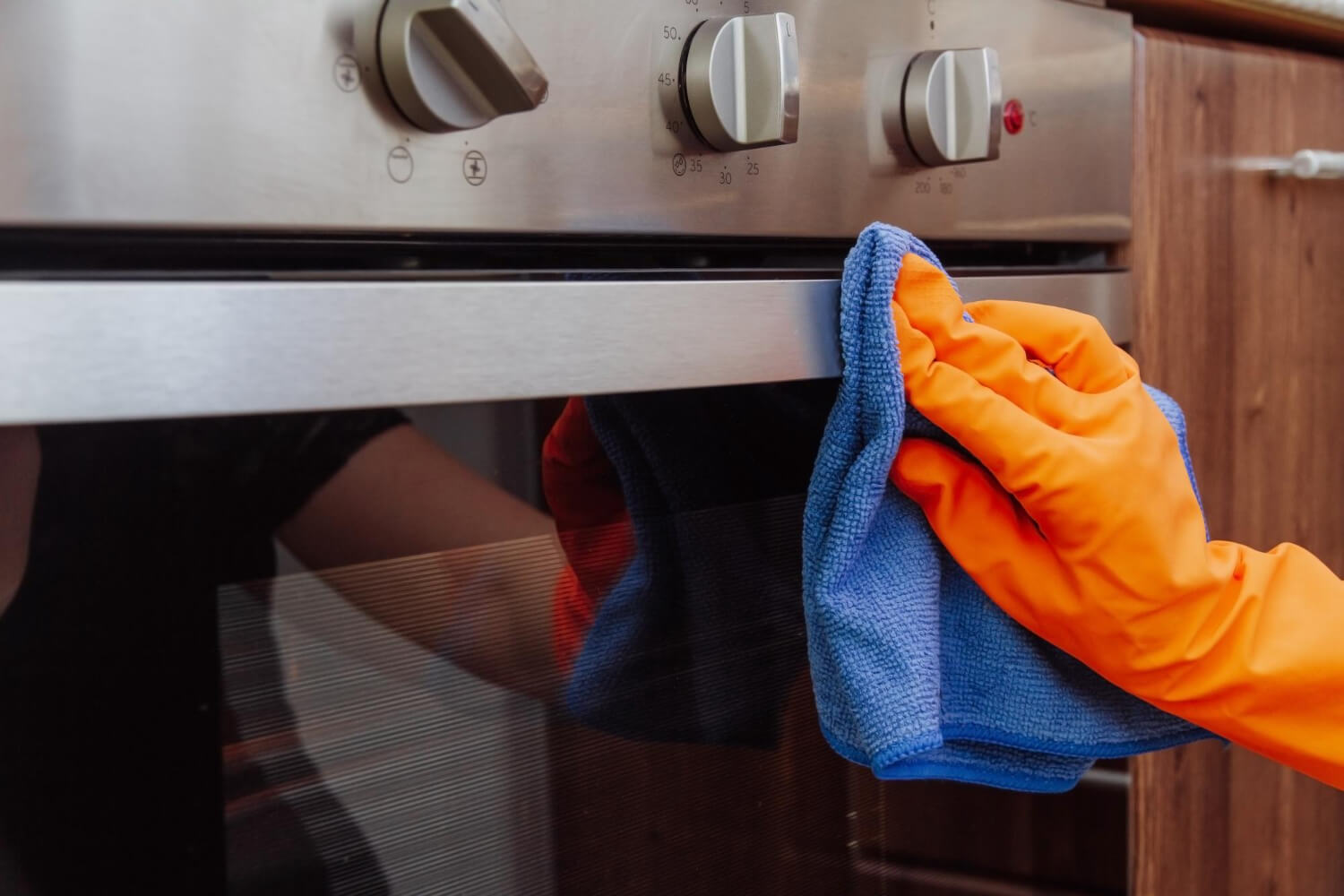man with orange gloves cleaning oven with microfiber cleaning cloth
