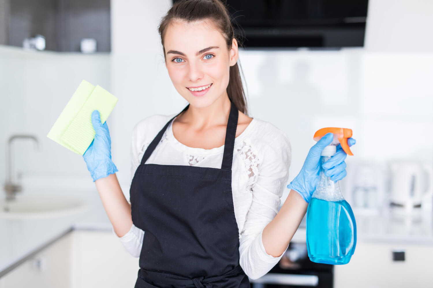 happy browned haired woman with blue eyes and black uniform smiling at camera while holding cleaning spray and cloth