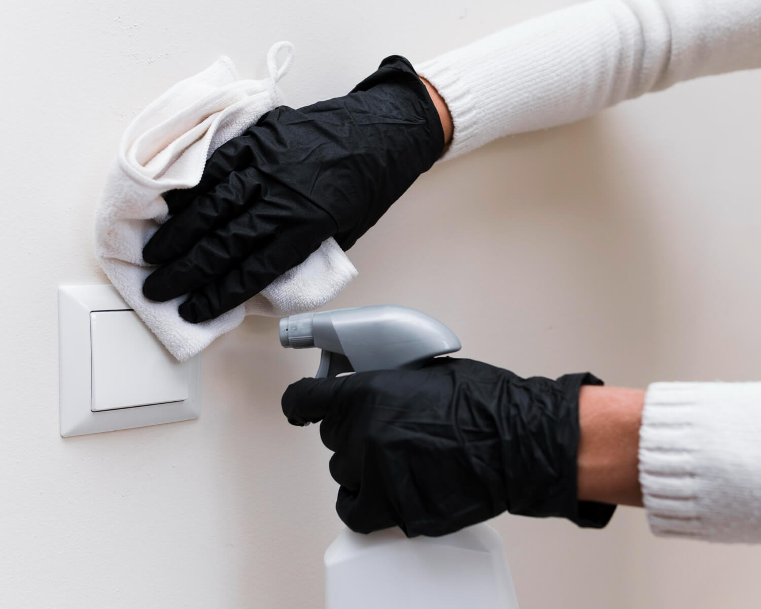 close up female hands in black protective gloves cleaning light switch with white cleaning spray and white cloth