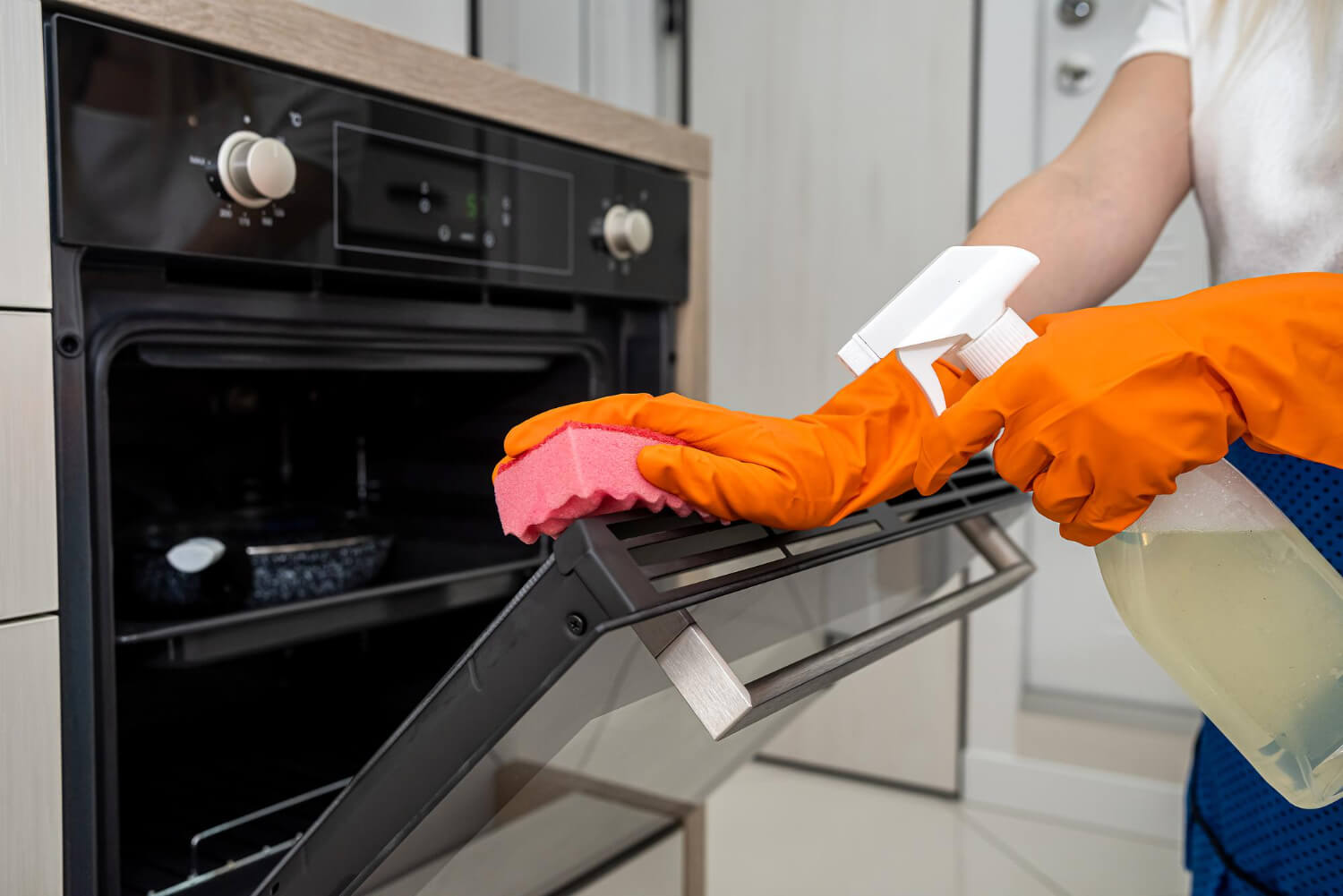 woman cleaning oven with orange glove
