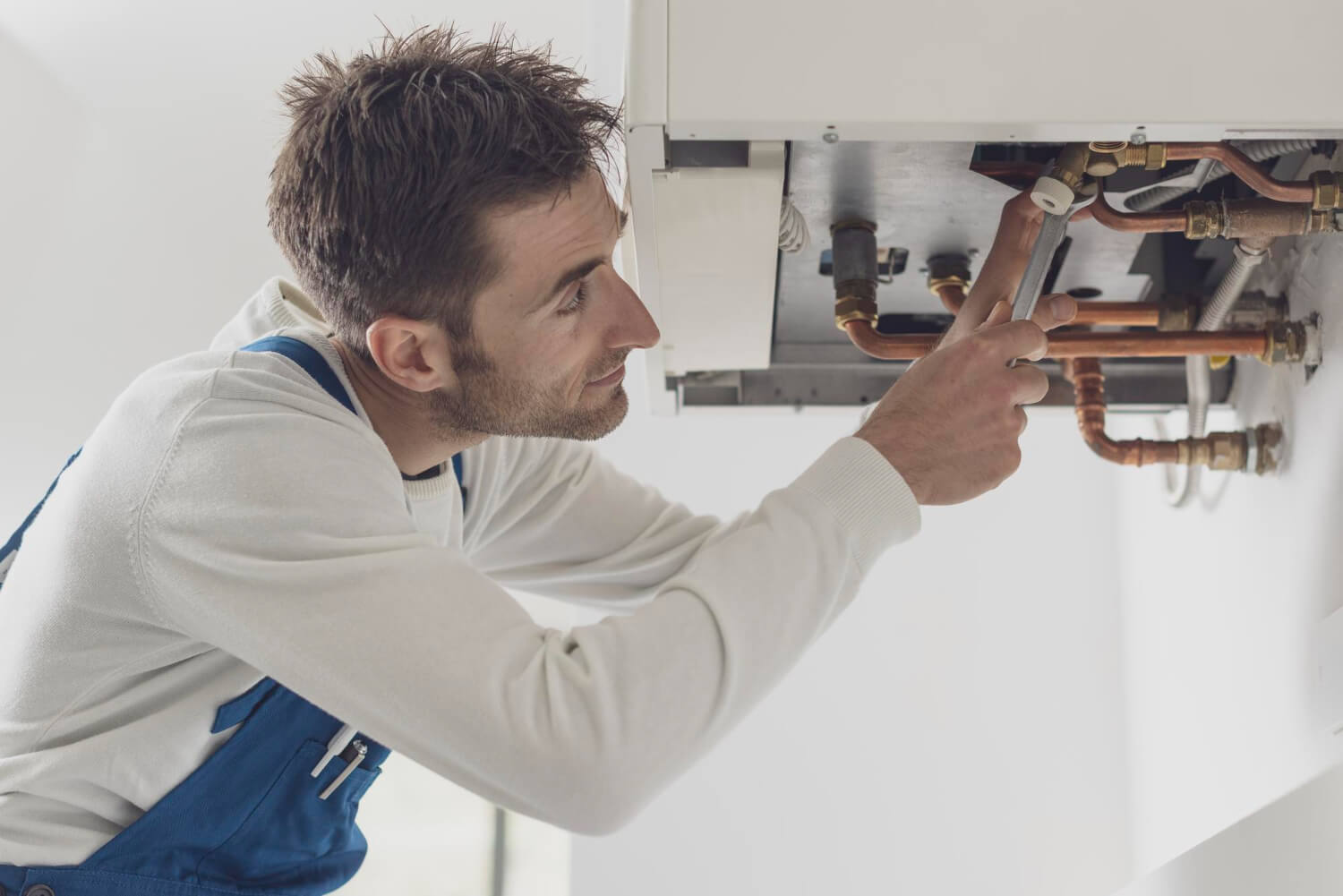side view of professional plumber in blue uniform trying to fix boiler