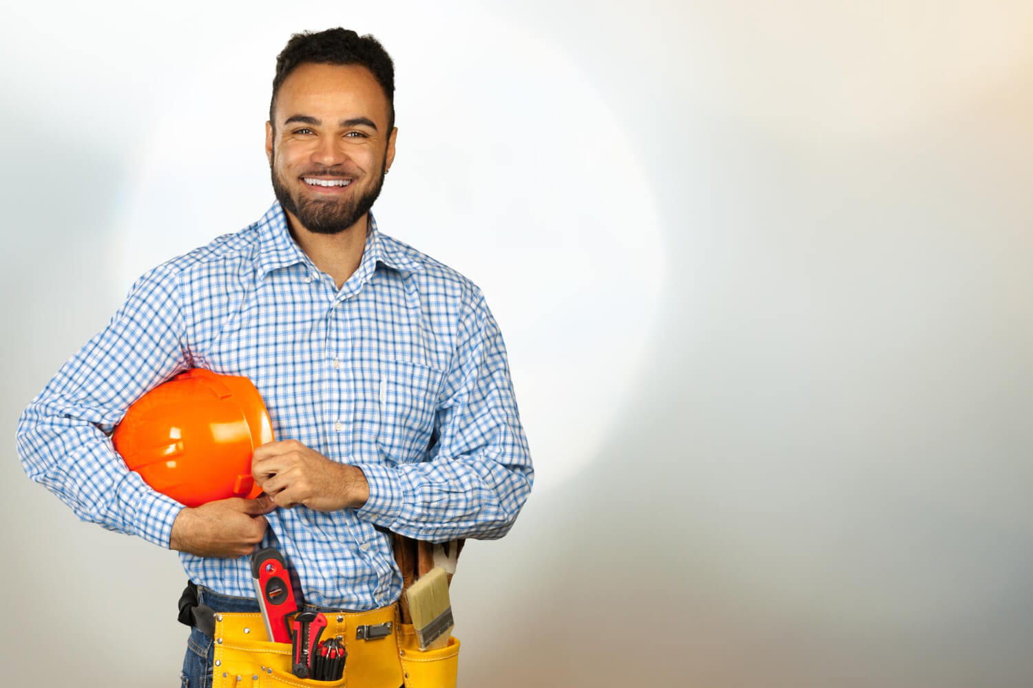 close up handyman smiling on camera while holding orange helmet