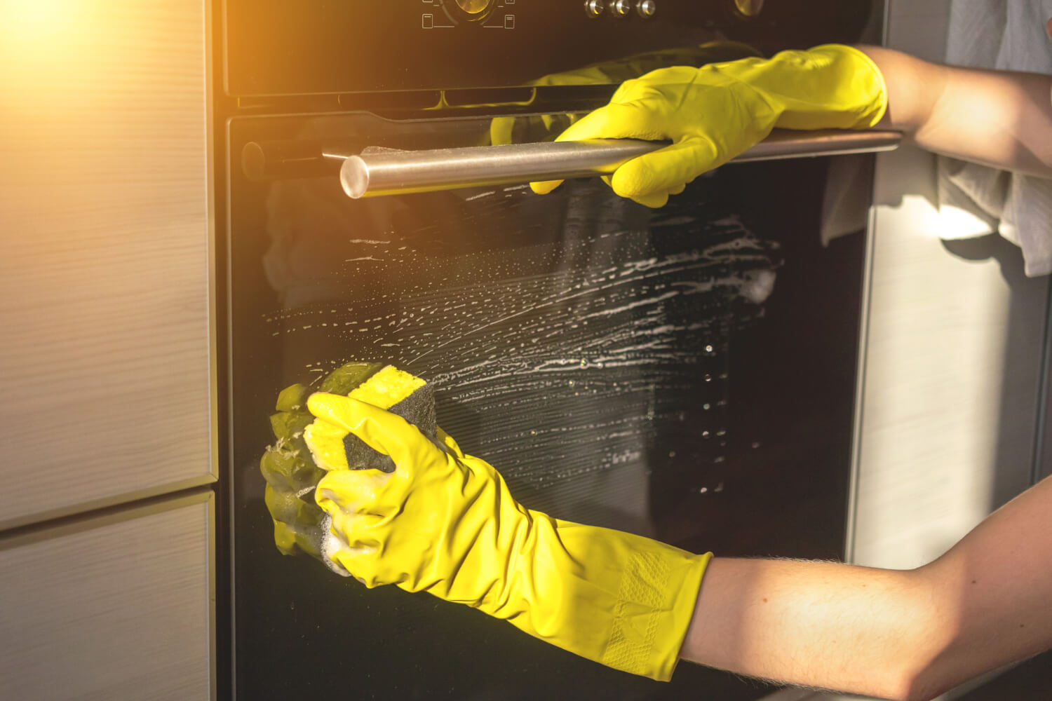 woman washing electric oven with ywllow rubber gloves and sponge on her hand
