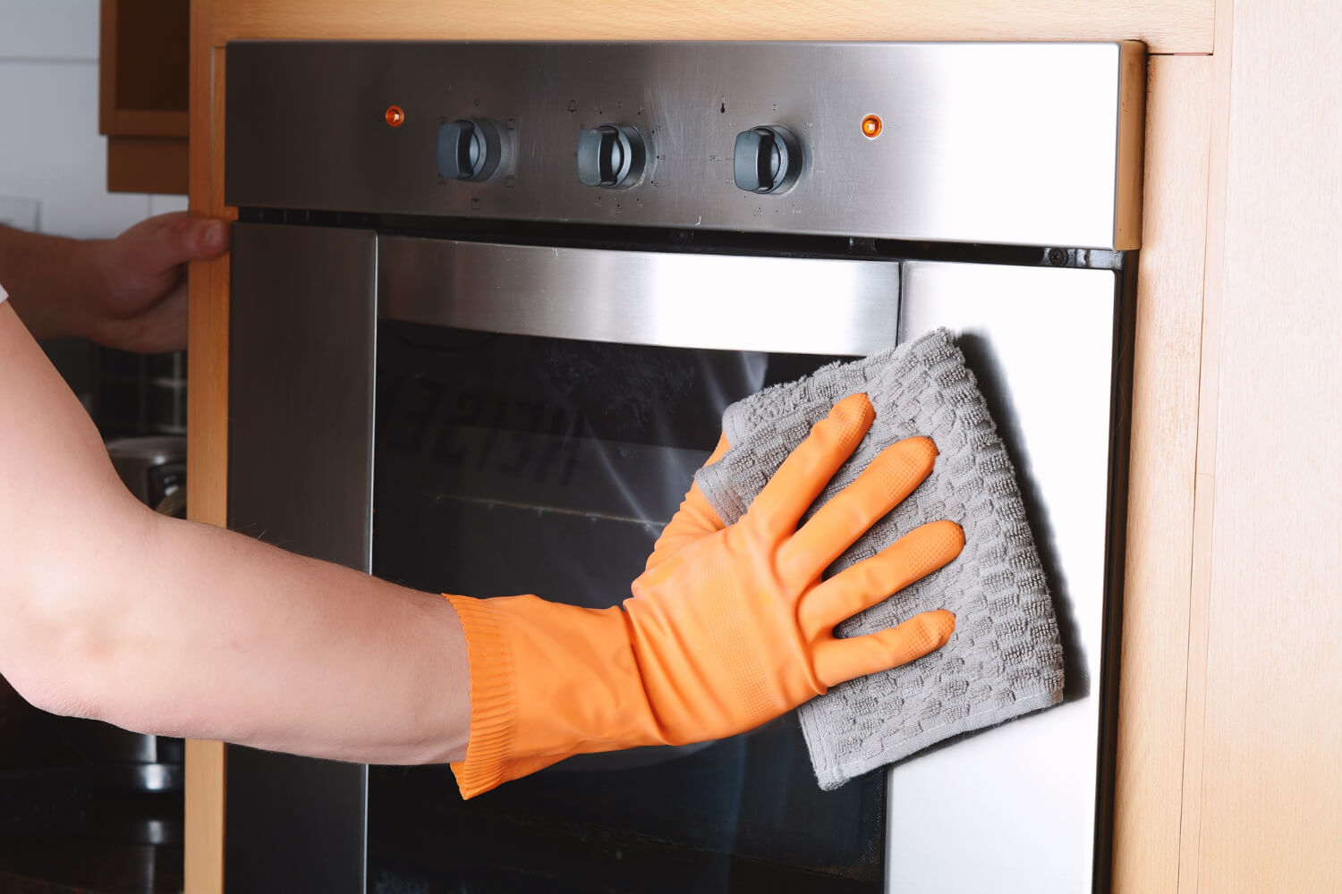 cleaner with orange gloves cleaning the outside of the oven close up