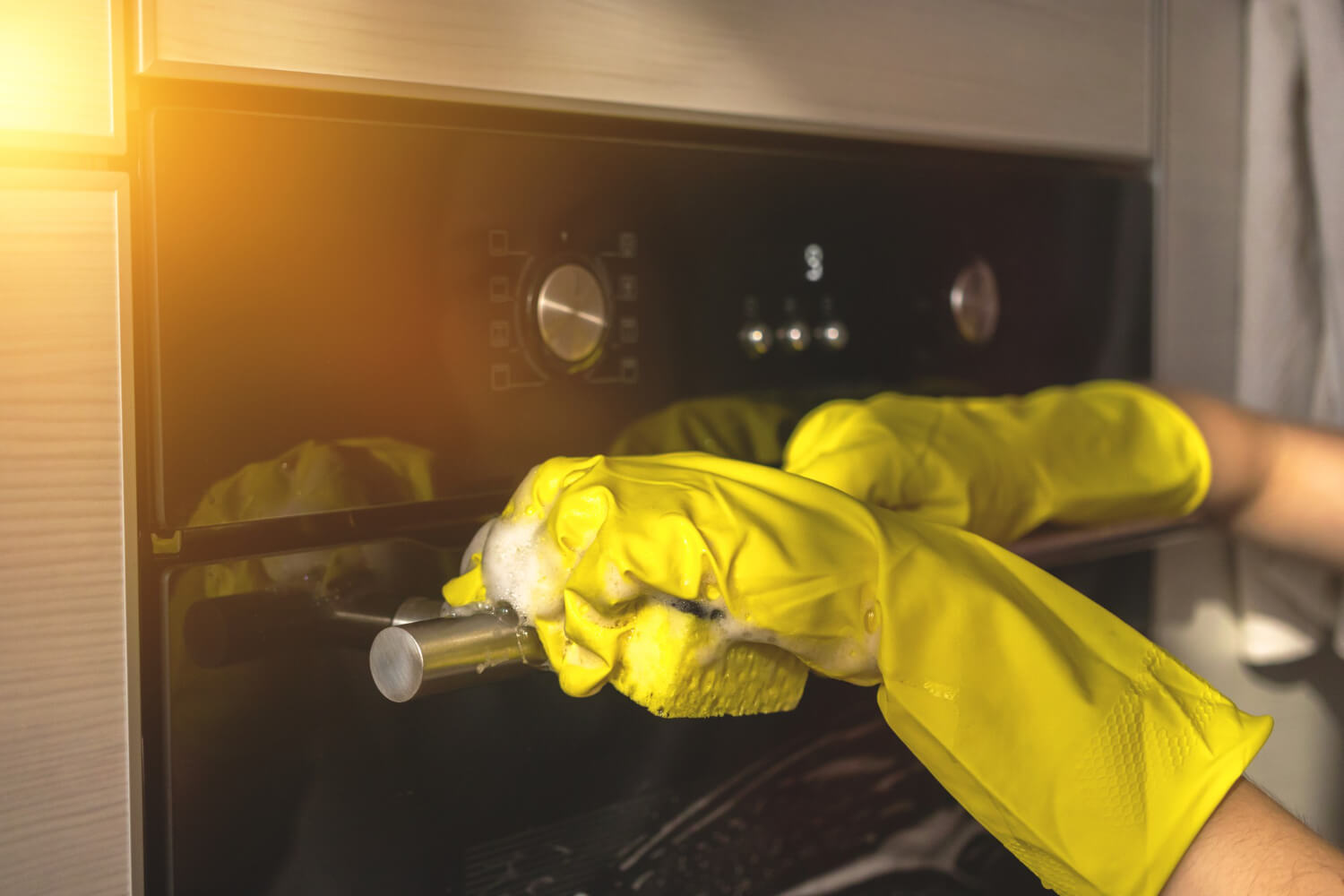 wiping cleaning oven door home kitchen with yellow rubber glove and sponge