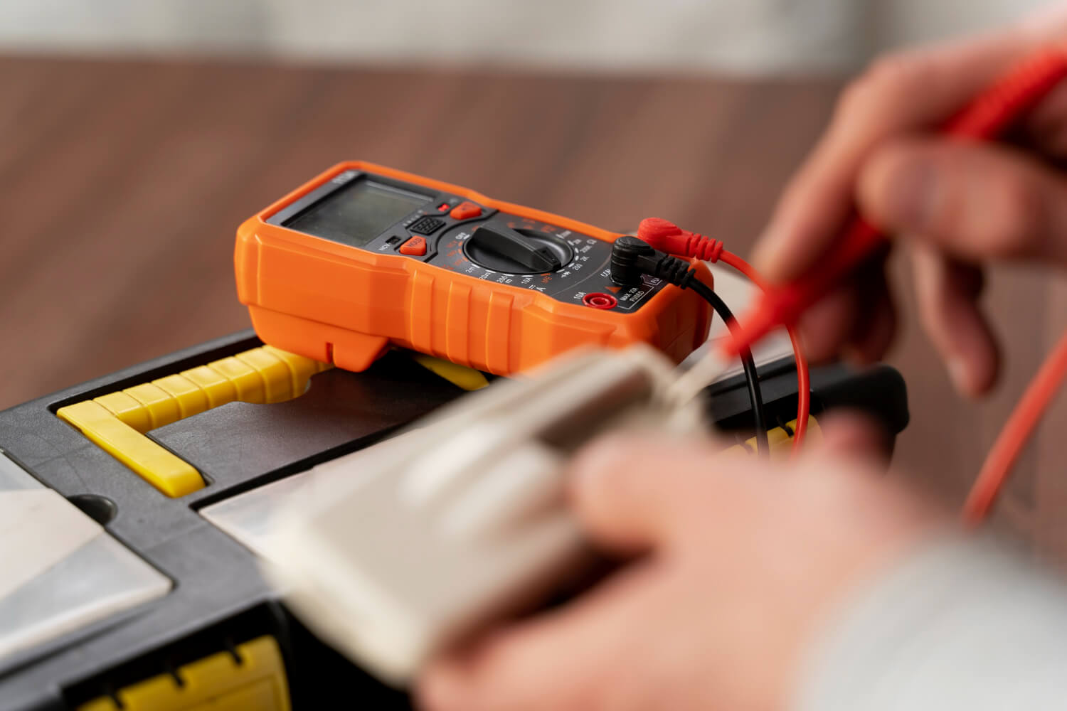 close up electricians hands performing portable appliance testing on blurred electric appliance