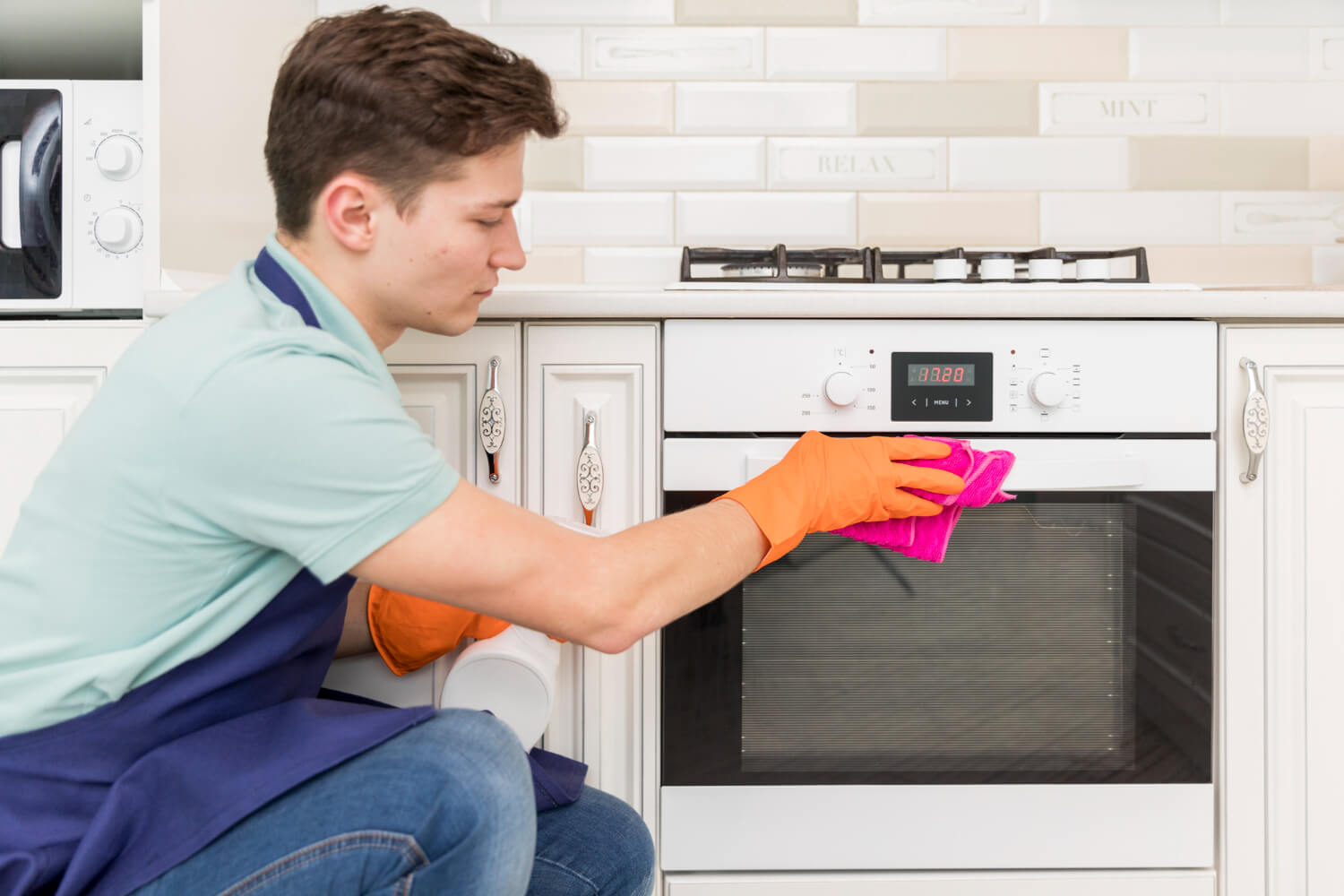 young man with orange gloves cleaning his oven