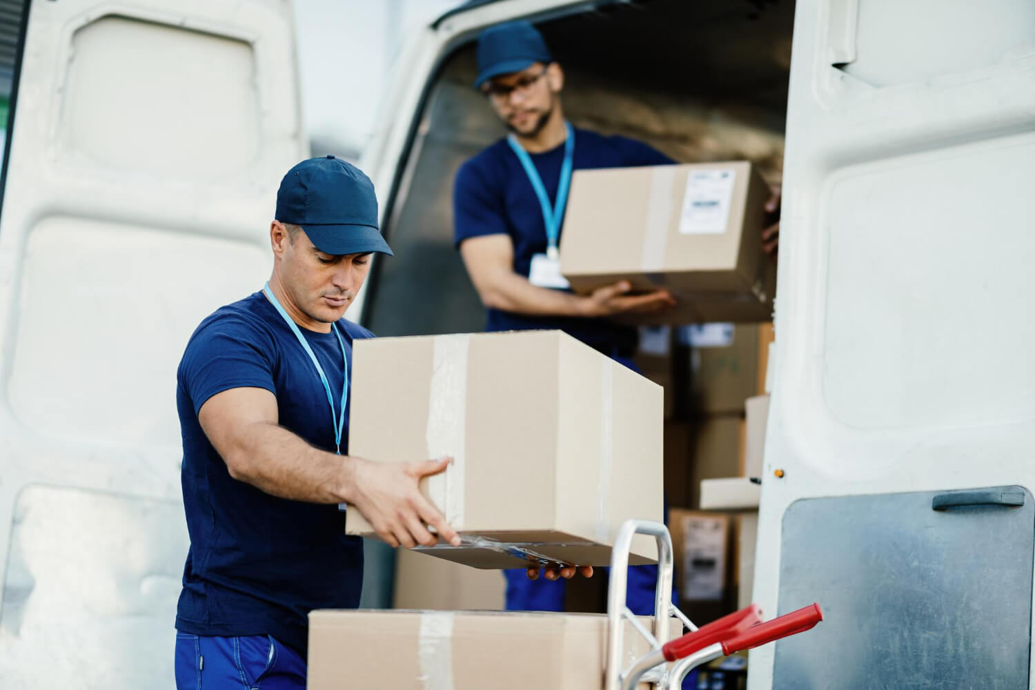 two movers unloading moving boxes from white moving van