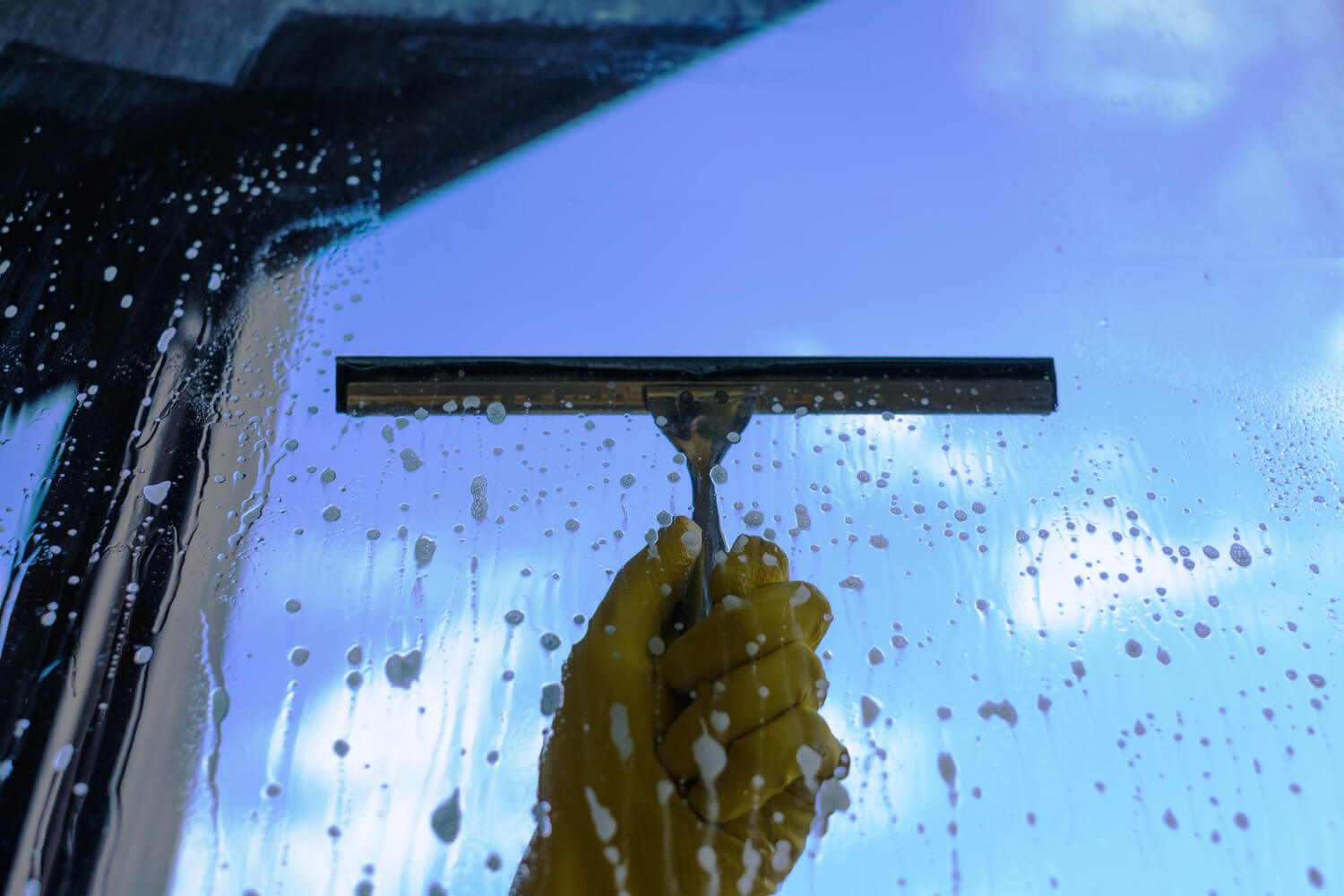 close up cleaners hand in yellow glove washing windows in the view of blue sky