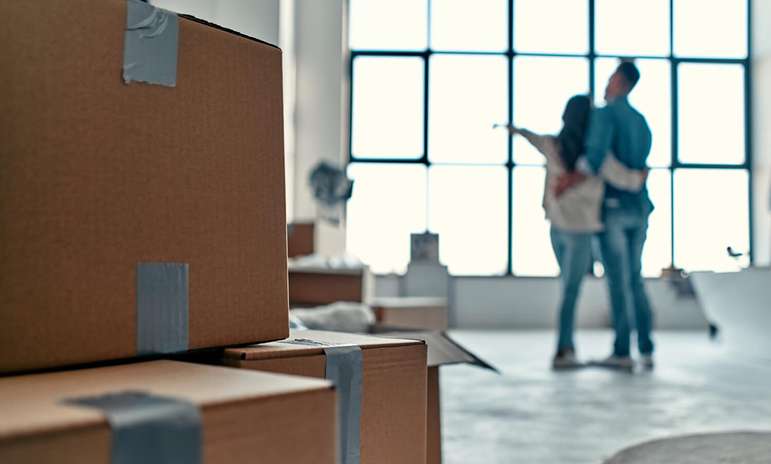 young couple blurred looking out of window with staffed moving boxes behind them