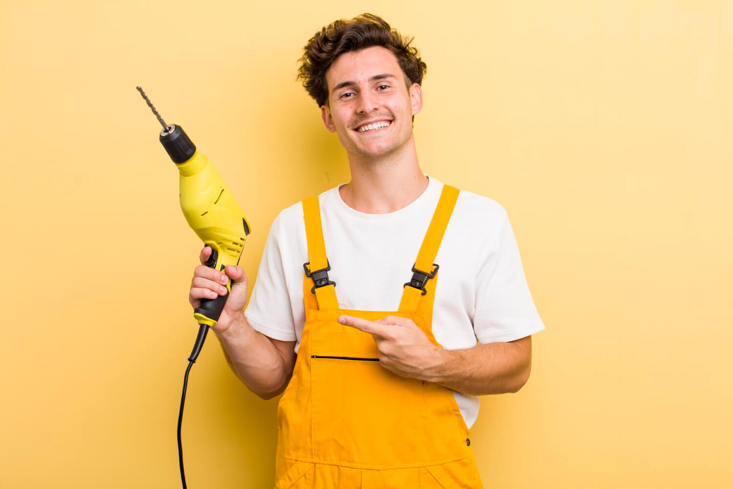 smiley handyman with yellow uniform holds drill and smiling on camera