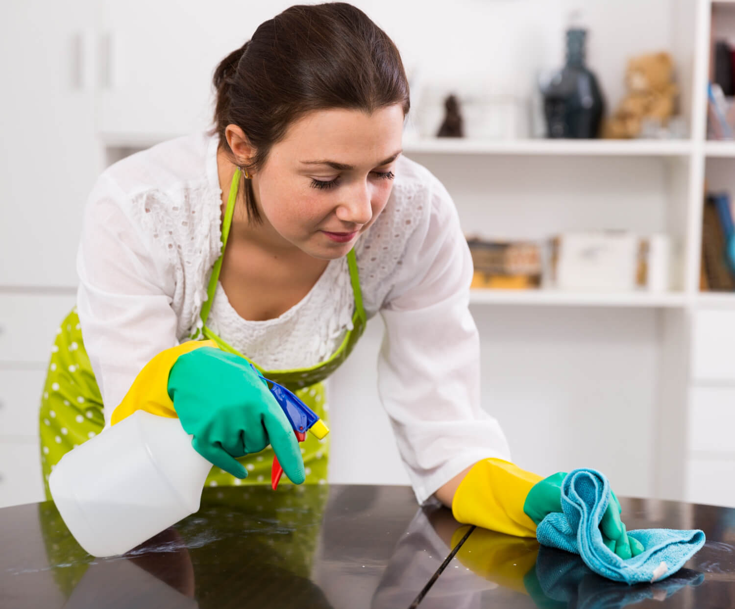 close up female cleaner in green gloves cleaning table with spray and blue cloth