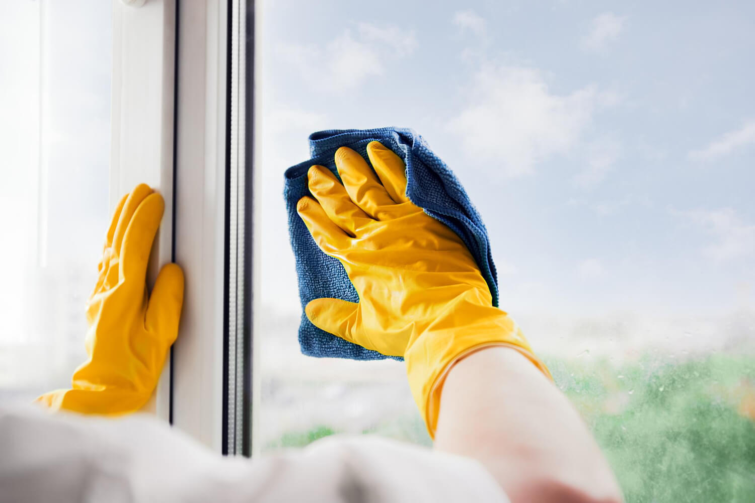 male cleaners hands close up in yellow gloves cleaning window glasse with b;ue squeegee