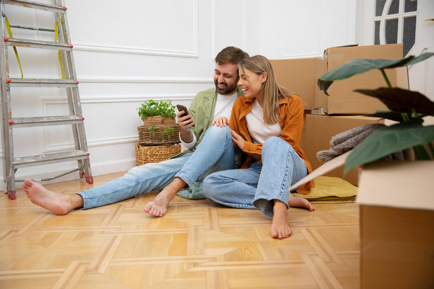 happy couple on the floor looking at phone with staffed moving boxes around them