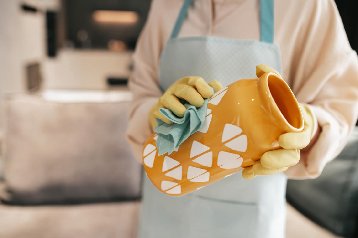 cropped female cleaner in yellow gloves close up cleaning orange vase with blue rag
