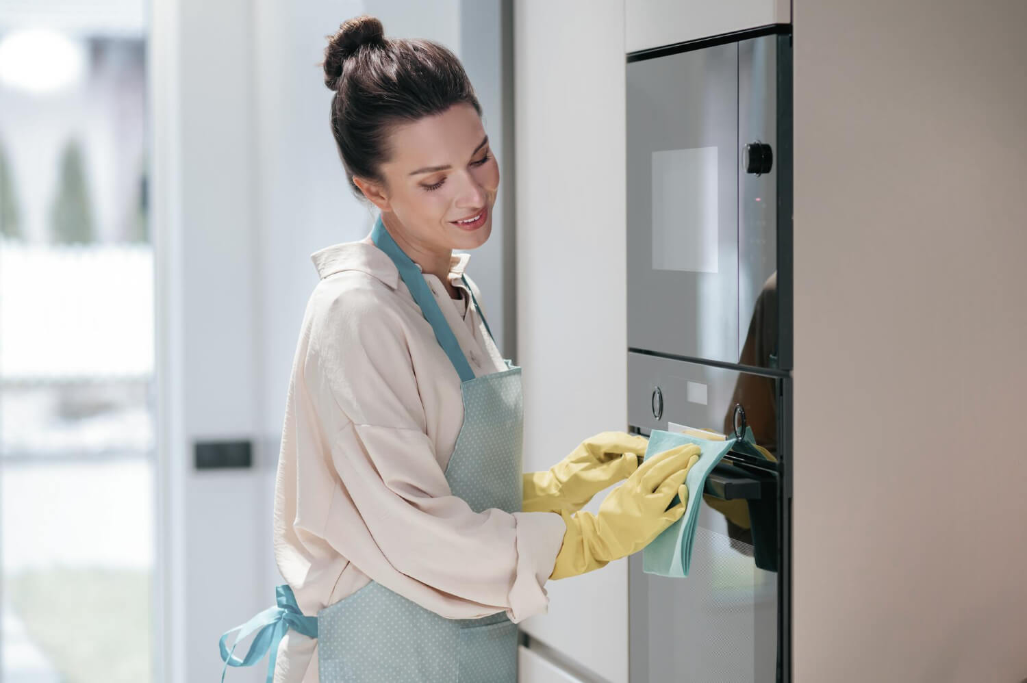 happy female cleaner cleans the outside part of oven door home kitchen with yellow rubber gloves
