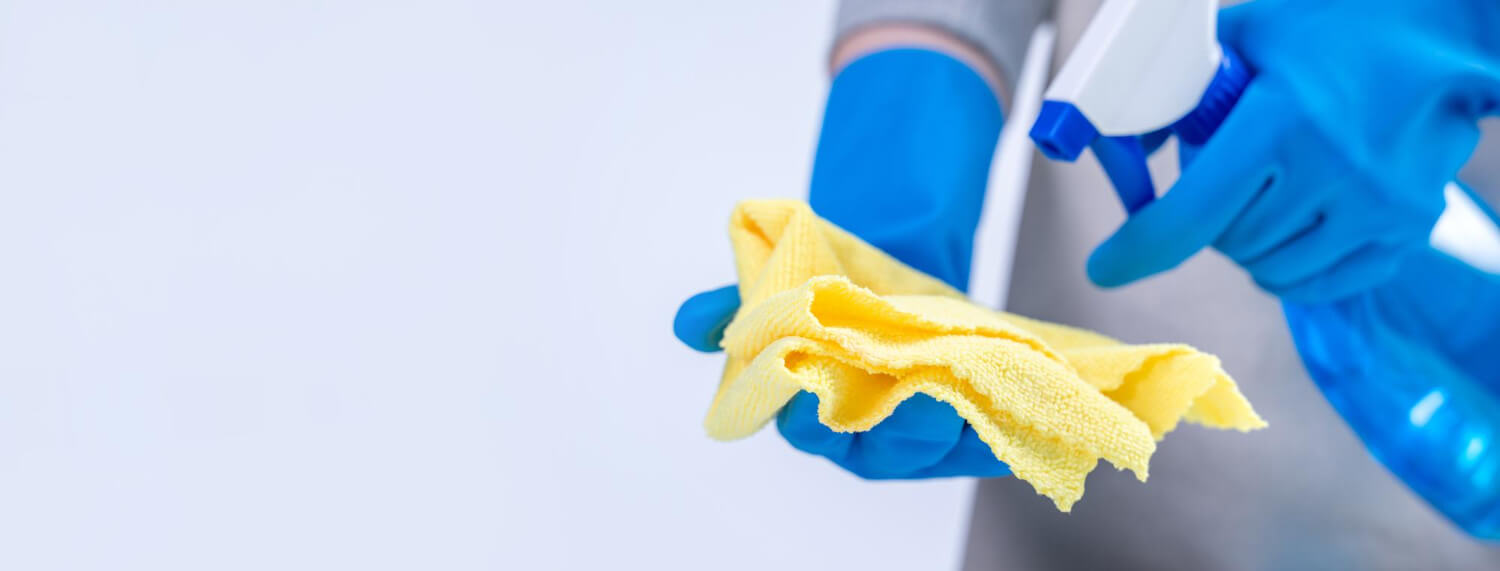 close up female cleaners hands in blue gloves spraying yellow cloth for cleaning