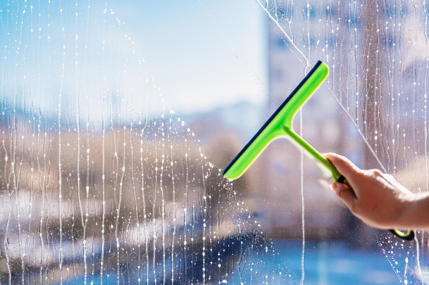 close up female hand cleaning squeegee for window cleaning with the blurred view of the city