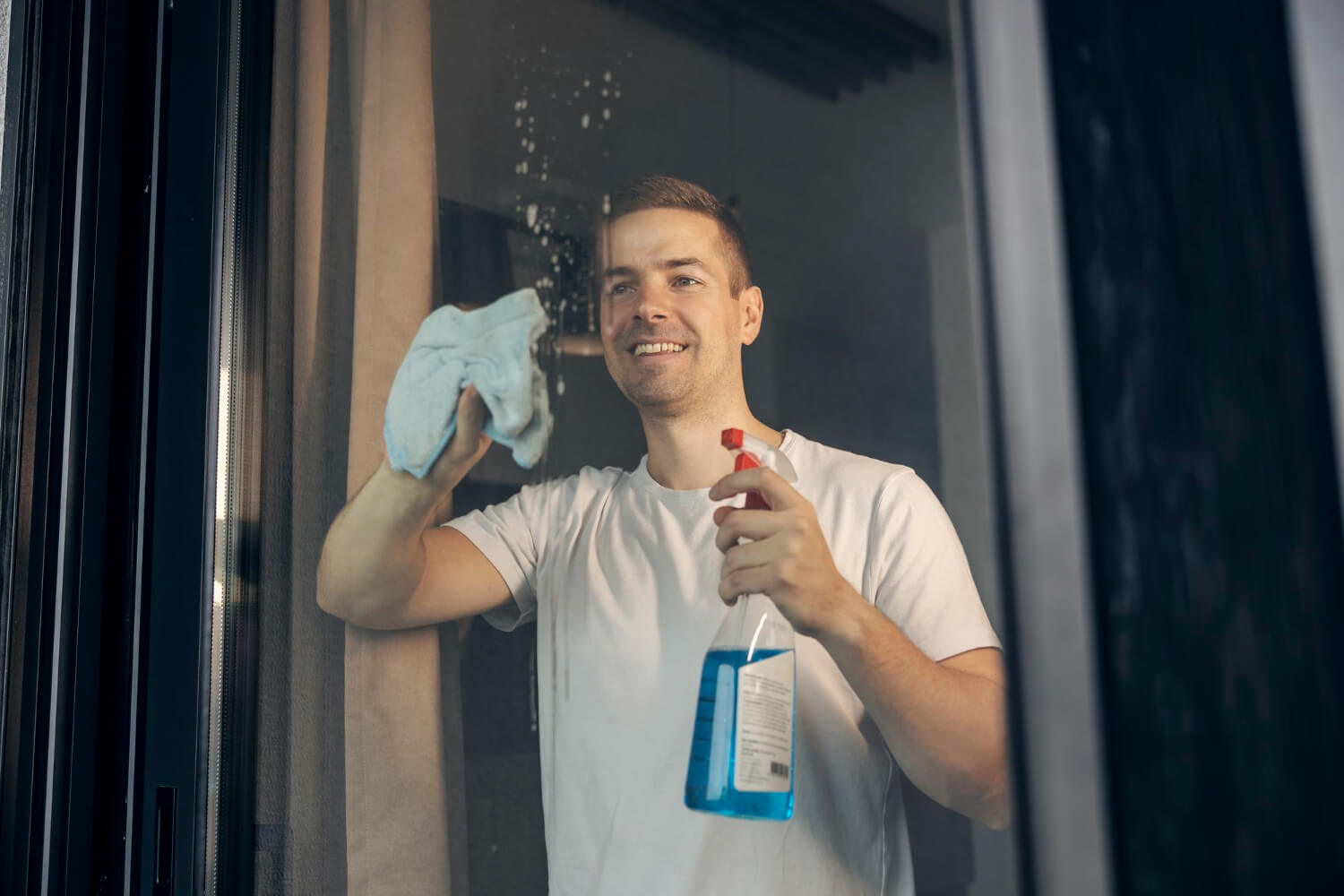 happy man spraying window detergent and rubbing with cloth