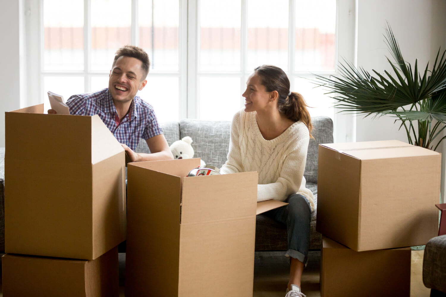 happy couple sitting on sofa having fun while unpacking boxes on moving day