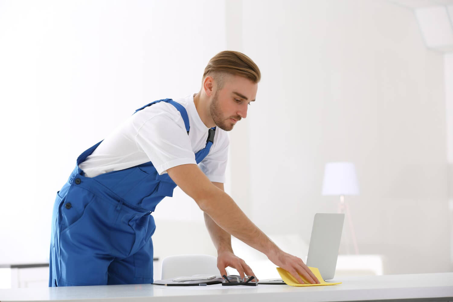 man close up male cleaner in blue uniform cleaning white office with yellow cloth