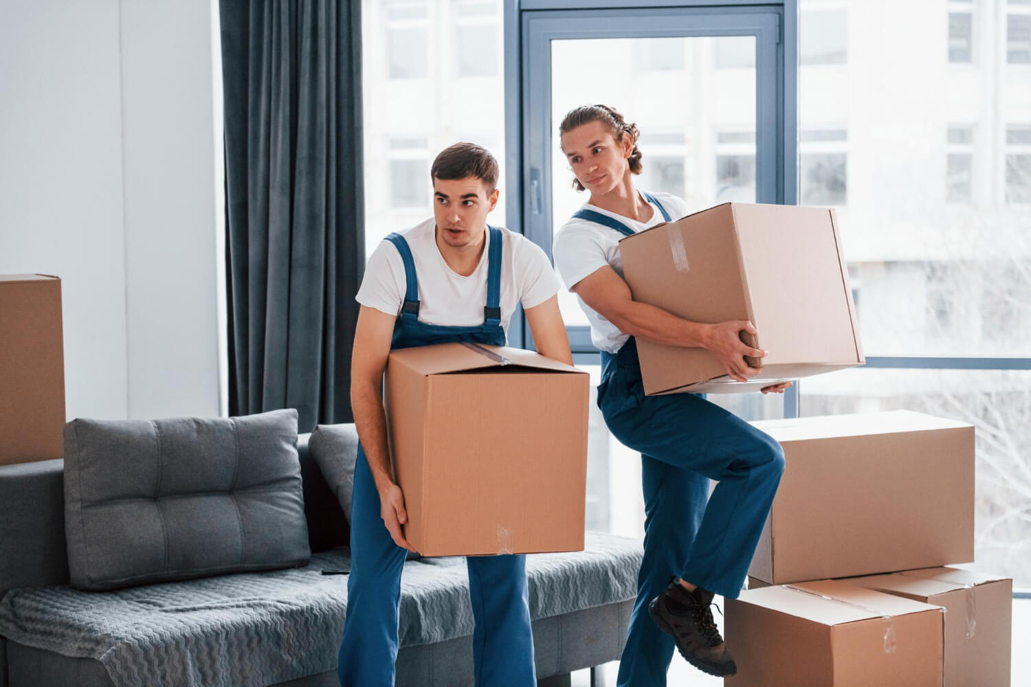 two young movers in uniforms carrying moving boxes from apartment