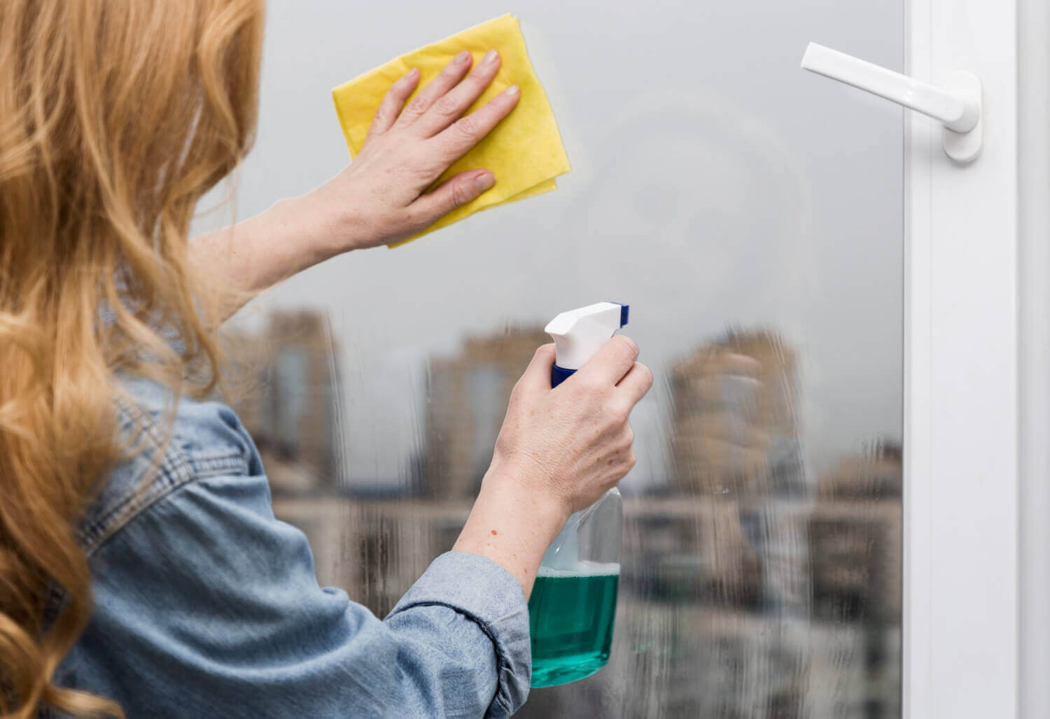 woman in shirt cleaning window with cleaning spray and yellow cloth