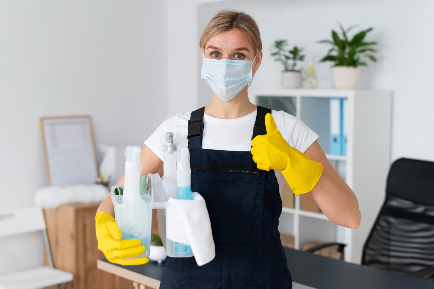 female cleaner close up with black uniform in yellow gloves holding bucket with cleaning equipment doing thumbs up in camera
