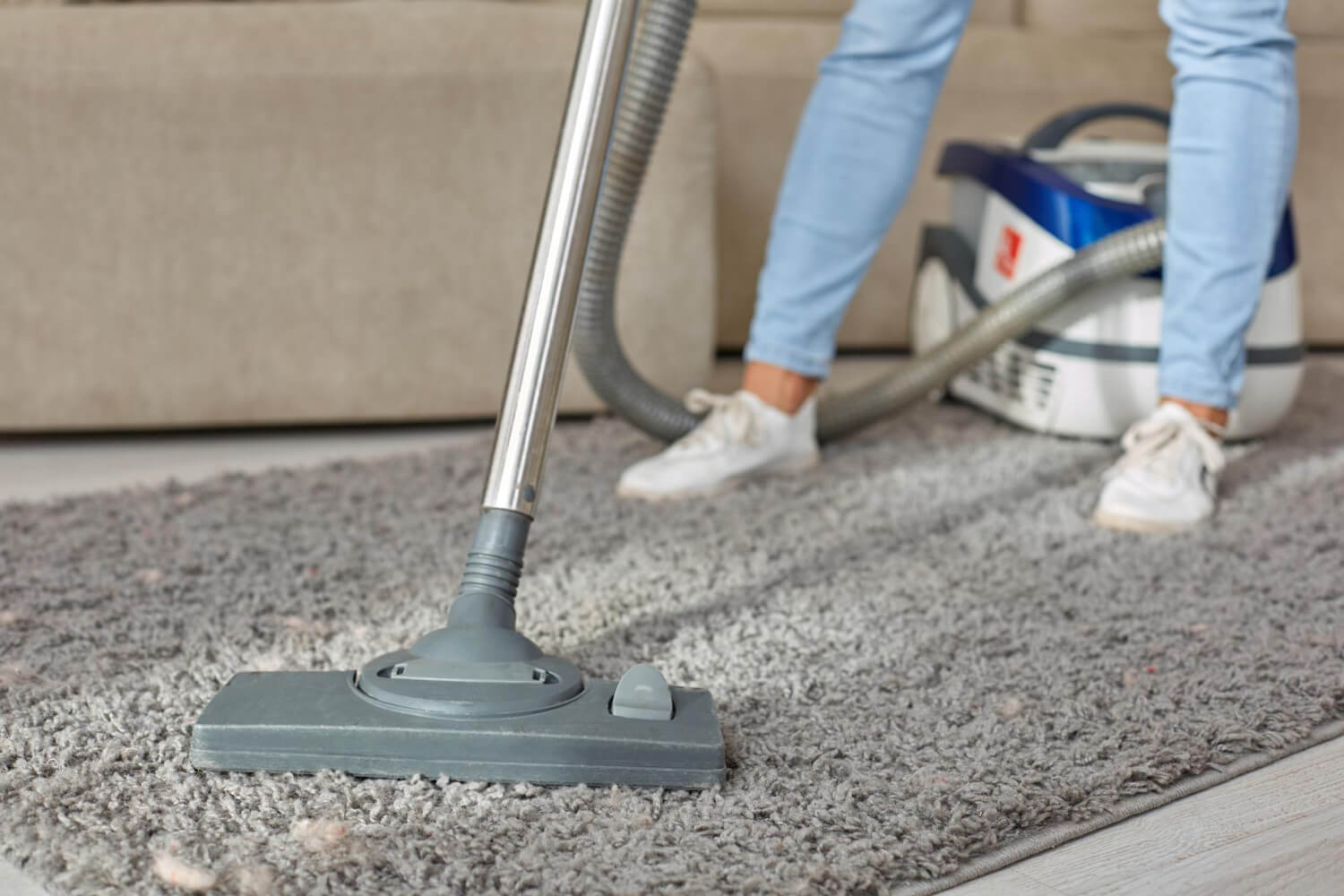 close up on vacuum cleaner used by female in sneakers while cleaning grey carpet